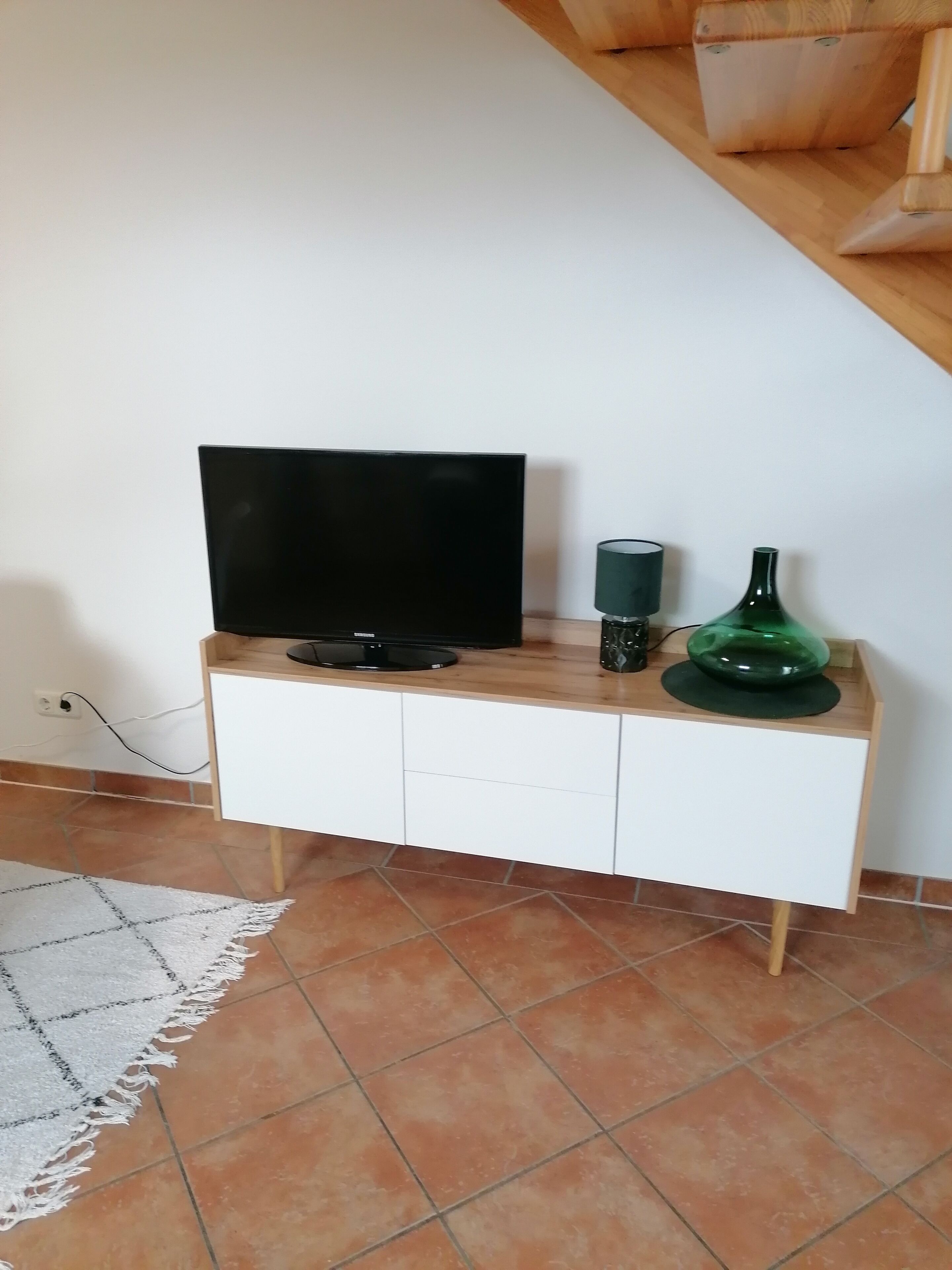 A TV on a wooden TV stand with a green vase and a lamp.