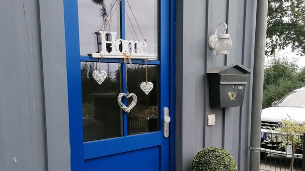 A blue door with a 'Home' sign, a potted plant, and a birdhouse on the wall.