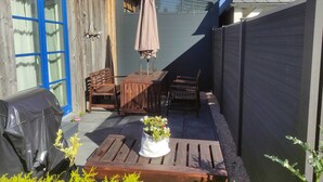 A patio with wooden furniture, a barbecue grill, and a potted plant.