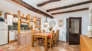 Una cuina amb prestatges de fusta, una taula de dinar amb caires, un rellotge i una porta amb un panell de vidre.