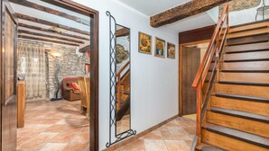 Un passadís amb una escala de fusta, una paret de pedra i un mirall que reflecteix l'espai.