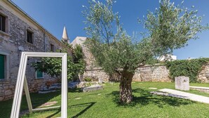 Edifici de pedra amb teulada cònica, un arbre al primer terme i un marc blanc recolzat contra l'edifici.