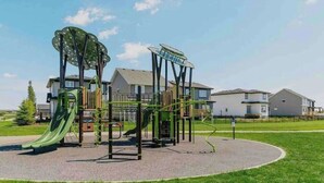 Ein Spielplatz mit verschiedenen Spielgeräten, darunter eine Rutsche und Kletterelemente, vor Wohngebäuden.