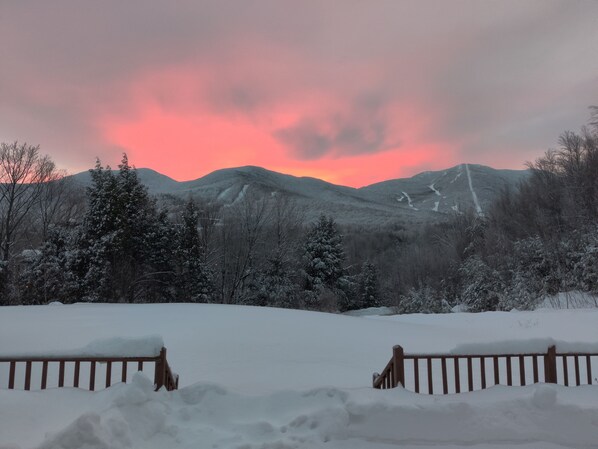 A snowy landscape with a wooden fence in the foreground and mountains in the background.