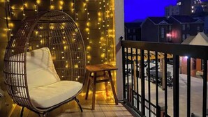 Uma varanda com uma cadeira suspensa, um banquinho de madeira e uma guirlanda de luzes.