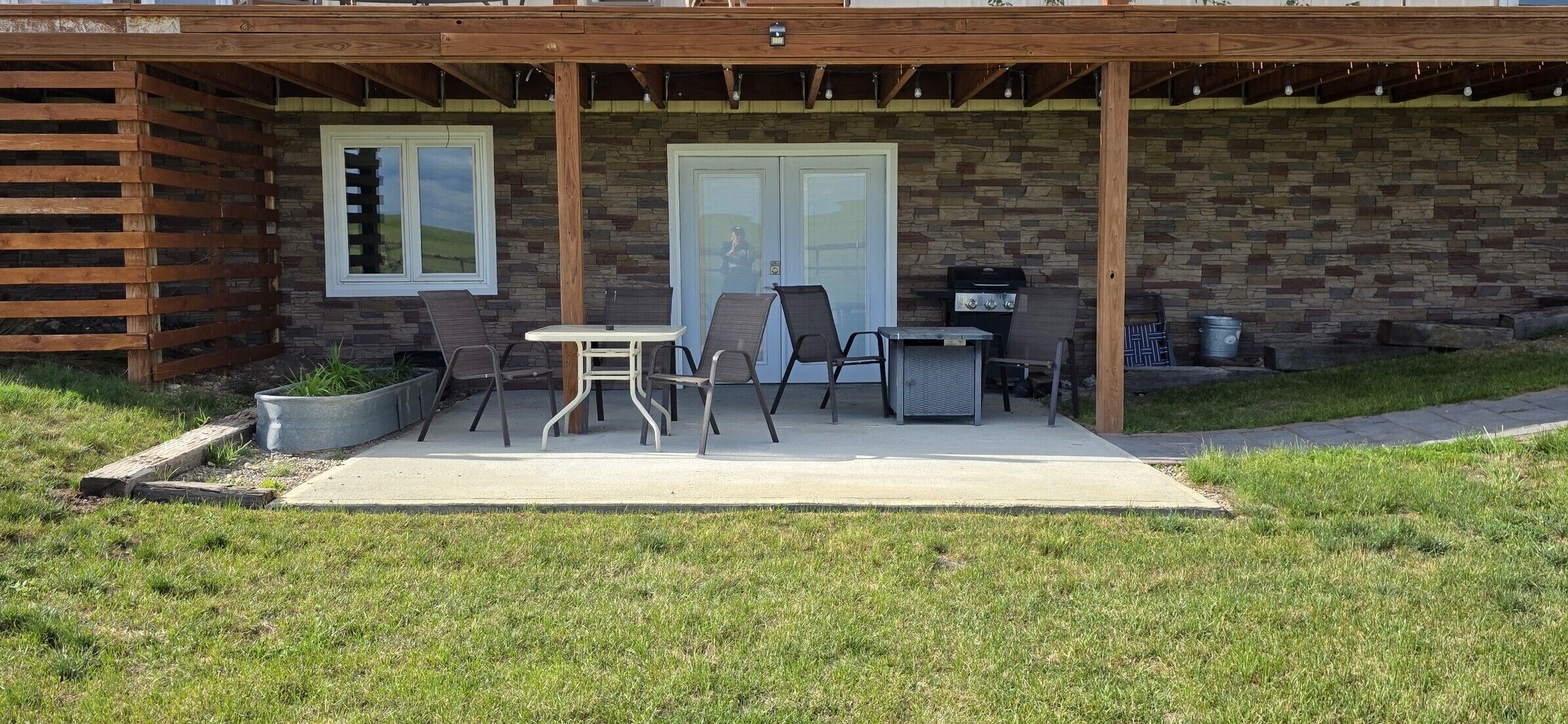 Une terrasse couverte avec un barbecue, deux portes et une table avec des chaises.