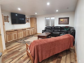 Un salon avec un meuble en bois, un canapé en cuir noir, une couverture rouge et un téléviseur à écran plat fixé au mur.