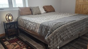Ein Schlafzimmer mit Bett, Nachttisch, Lampe, Fenster und Holztür.