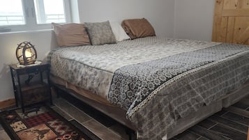 A bedroom with a bed, a nightstand, a lamp, a window, and a wooden door.