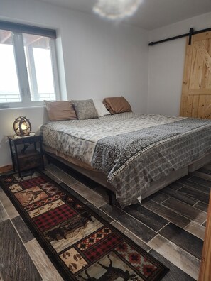 Une chambre à coucher avec un lit, une table de chevet, une lampe, une fenêtre et une porte en bois.