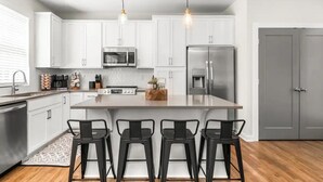 Una cocina moderna con armarios blancos, electrodomésticos de acero inoxidable y taburetes de bar negros.