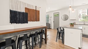 Una cocina moderna con barra de madera, taburetes negros y una gran obra de arte abstracto en la pared.