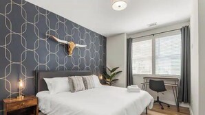 Un dormitorio moderno con una cama grande, un adorno de pared con un cráneo de vaca, un escritorio y una ventana con persianas.
