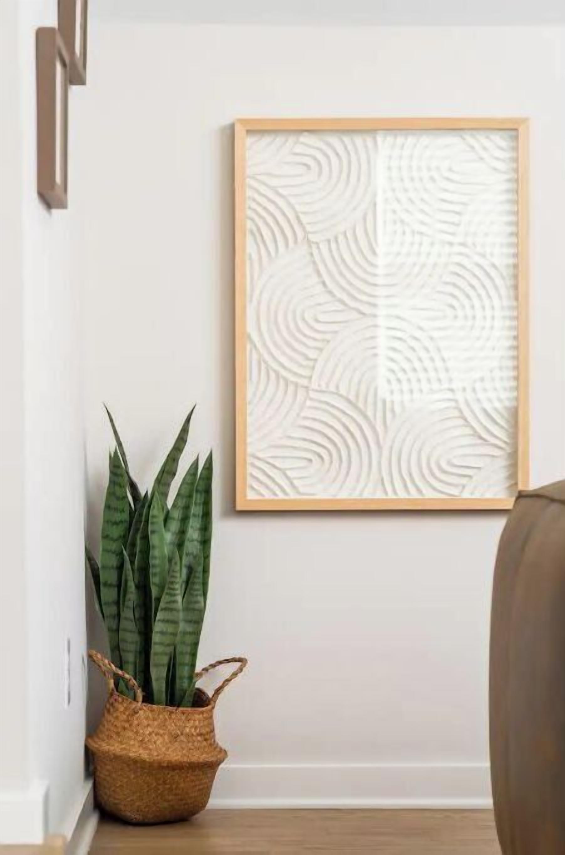 A framed artwork with a leaf pattern, a potted plant, and a woven basket on a wooden floor.