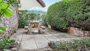 A patio with a table and chairs, a striped umbrella, and a thatched-roof building.