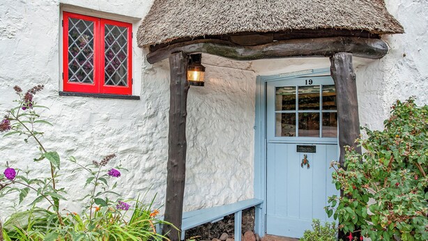 A traditional cottage with a blue door, a red window, and a thatched roof.