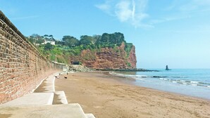 A beach with a stone wall, a rocky cliff, and a lighthouse in the distance.