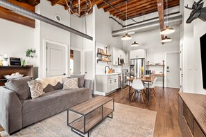 A modern interior with a grey sofa, a wooden dining table, and a kitchen area with white cabinets and stainless steel appliances. - ☆ New Rustic Loft ☆ Pool & 2 mi to Broadway & DT! (Nashville)