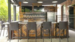 Un área de bar al aire libre con mostrador de madera, taburetes y una televisión montada.