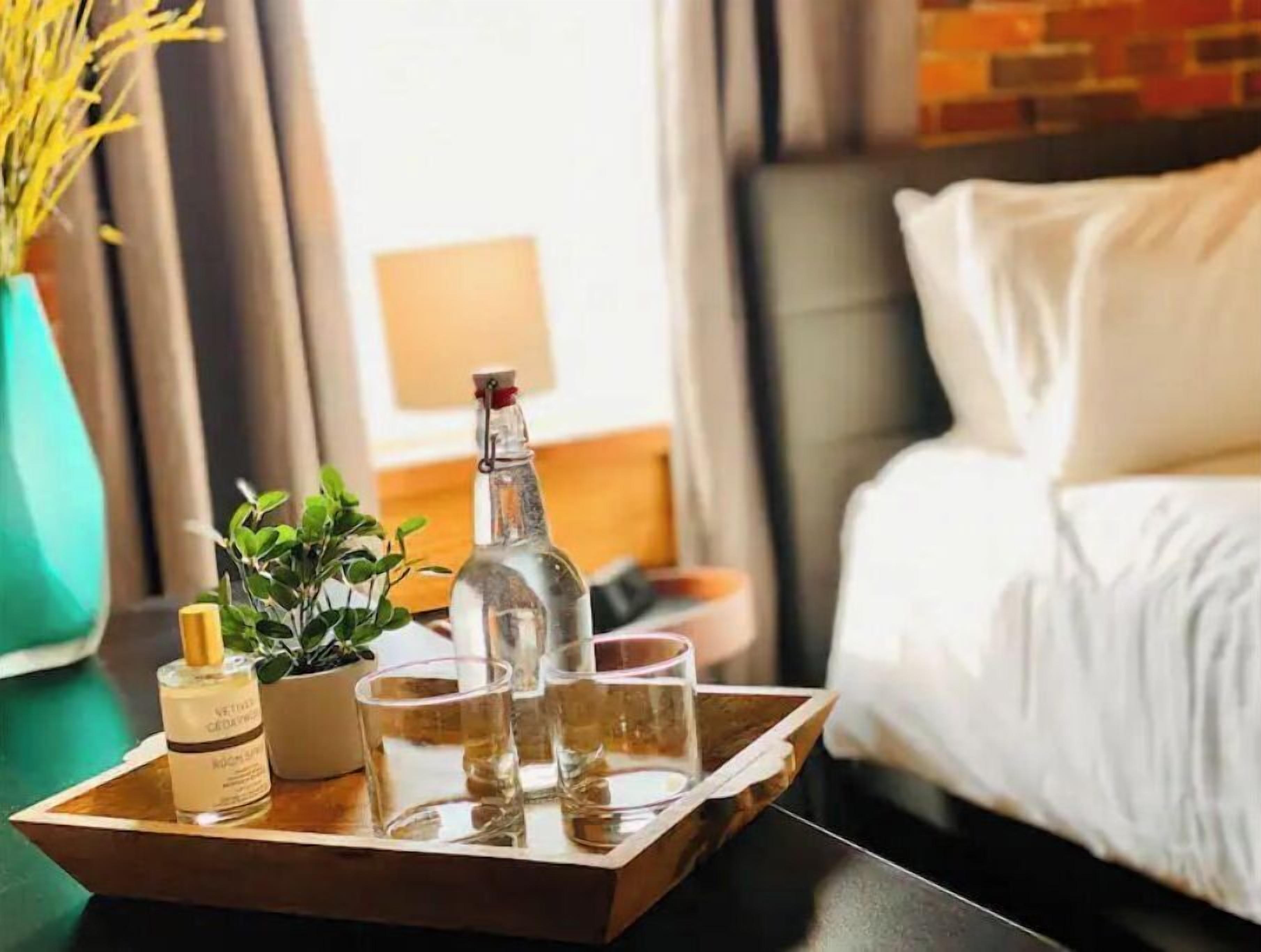A tray with a bottle, a small plant, and glasses on a table in a hotel room.