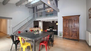 Une salle à manger spacieuse avec un plafond haut et des poutres apparentes, un escalier menant à un niveau supérieur et une grande armoire en bois.