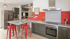 Une cuisine moderne dotée d’appareils électroménagers en acier inoxydable, d’un agencement aux couleurs rouge et blanc, et de tabourets de bar rouges.