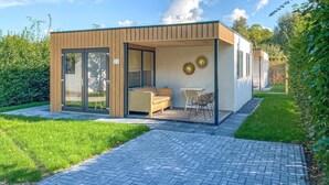 Een moderne, compacte buitenruimte met glazen deuropening, een bank, een klein tafeltje en decoratieve wandkunst.