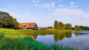Een klassiek Nederlandse boerderij met een grote schuur en een vijver op de voorgrond.