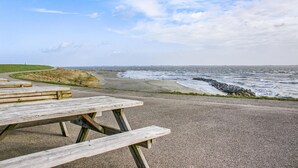 Een picknicktafel aan een verhard pad, dichtbij de zee met een rotsachtige kustlijn en een grasheuvel op de achtergrond.