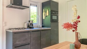 Een moderne keuken met een gasfornuis, koffiezetapparaat en een spoelbak. Er is een raam met uitzicht op groen.