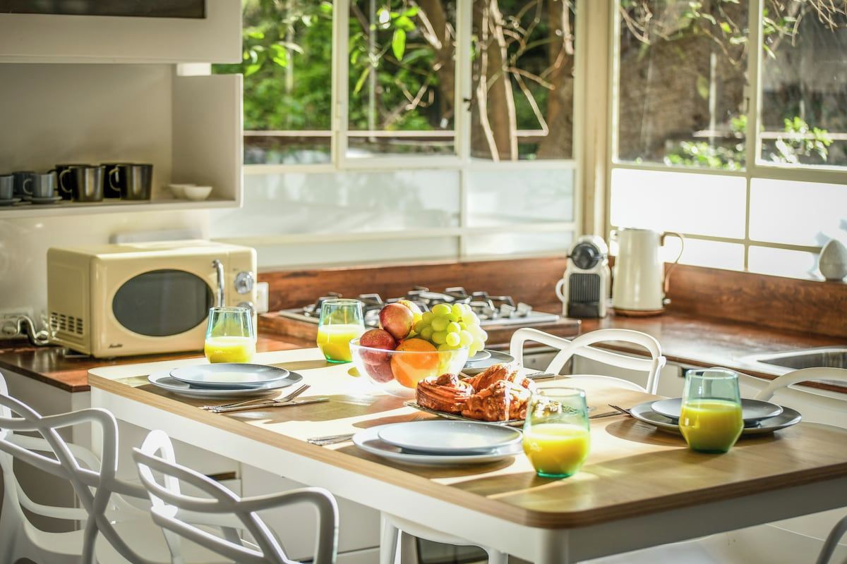 A breakfast setting with a table set for two, including plates, cutlery, and a bowl of fruit.