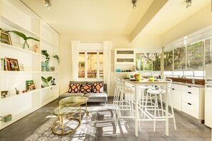 A modern kitchen with white cabinetry, a dining area with white chairs, and a sofa with patterned cushions.