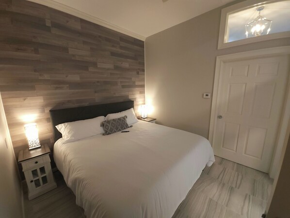 A neatly arranged bedroom with a wooden headboard, a bedside table with a lamp, and a door.