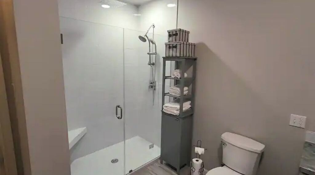 Un baño moderno con ducha de vidrio, inodoro y estante con toallas.