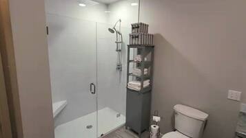 Un baño moderno con ducha de vidrio, inodoro y estante con toallas.