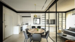 A modern kitchen with white cabinets, a dining area with a round table and chairs, and a living area with a sofa and coffee table. - Stylish 2BR with Refined Design & Balcony Charm (Tel Aviv-Yafo)