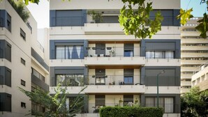A multi-story residential building with balconies, a central entrance, and a clear sky. - Stylish 2BR with Refined Design & Balcony Charm (Tel Aviv-Yafo)