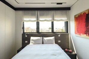 Un letto con biancheria bianca, una testiera e due comodini con oggetti rosa sopra.