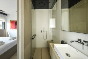 Un bagno moderno con doccia, uno specchio grande e un lavandino bianco.