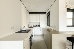 A modern kitchen with white cabinetry, a black countertop, and a window with blinds.