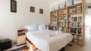 A bedroom with a large bed, a bookshelf, and a suitcase. - Bright 3BR Stay • Relaxing Comfort (Tel Aviv-Yafo)