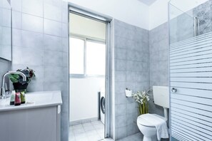 Un bagno moderno con una parete piastrellata di grigio, un lavabo bianco con articoli da toilette, un water e una zona doccia.