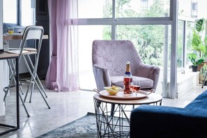 Un soggiorno moderno con un'ampia finestra, una poltrona grigia, un tavolino rotondo e un divano blu.