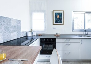 Une cuisine moderne avec un poêle noir, des armoires blanches et une fenêtre donnant sur des immeubles.