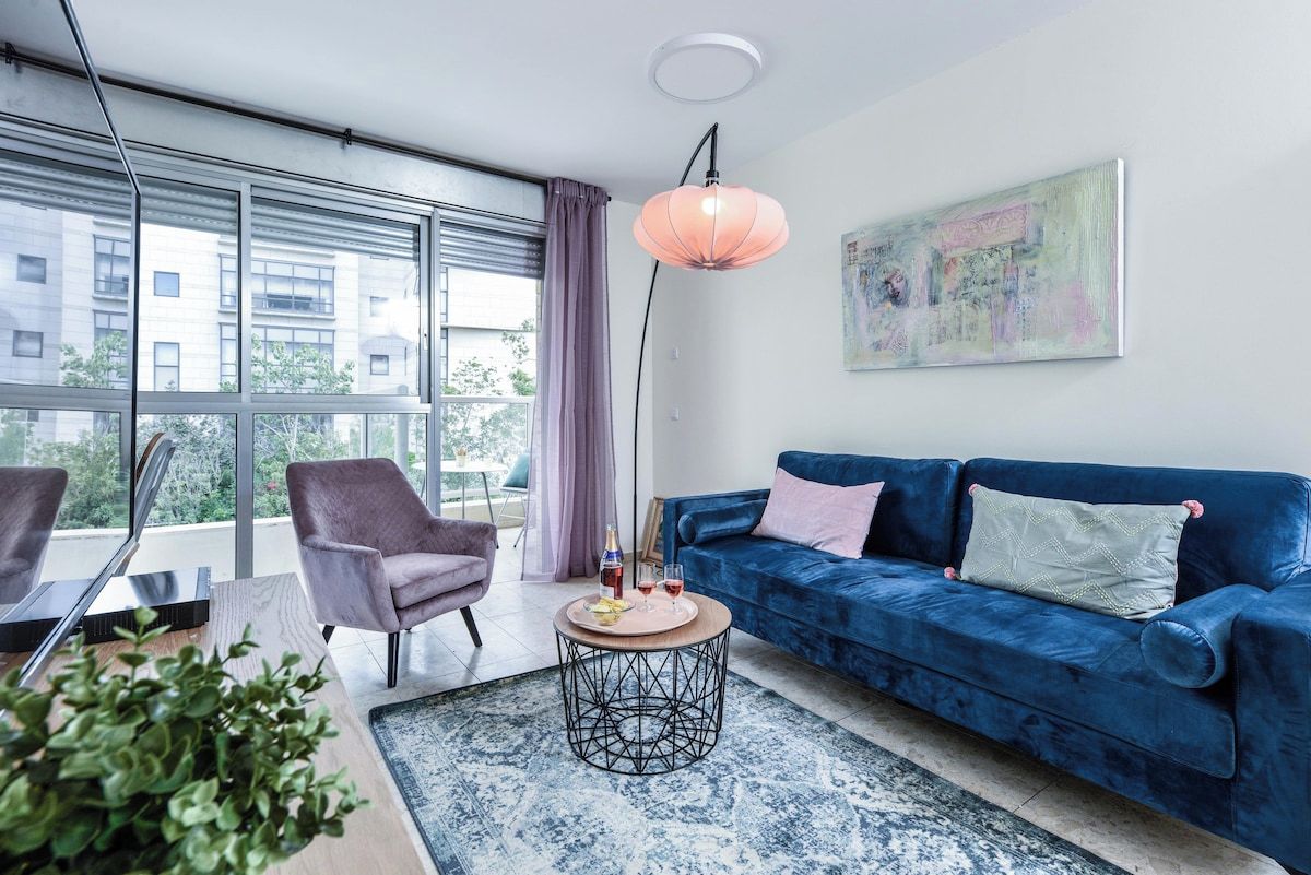 A modern living room with a blue sofa, a round coffee table, and a large window with blinds.