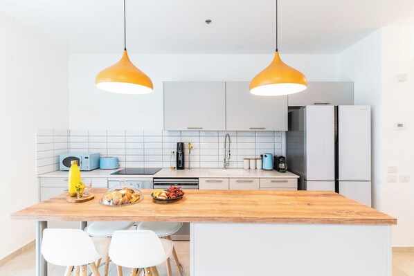 Une cuisine moderne avec un îlot central en bois, des armoires blanches et deux suspensions lumineuses.