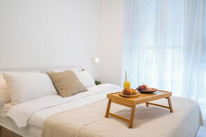A bedroom with a bed, a bedside table with breakfast items, and a window with sheer curtains.