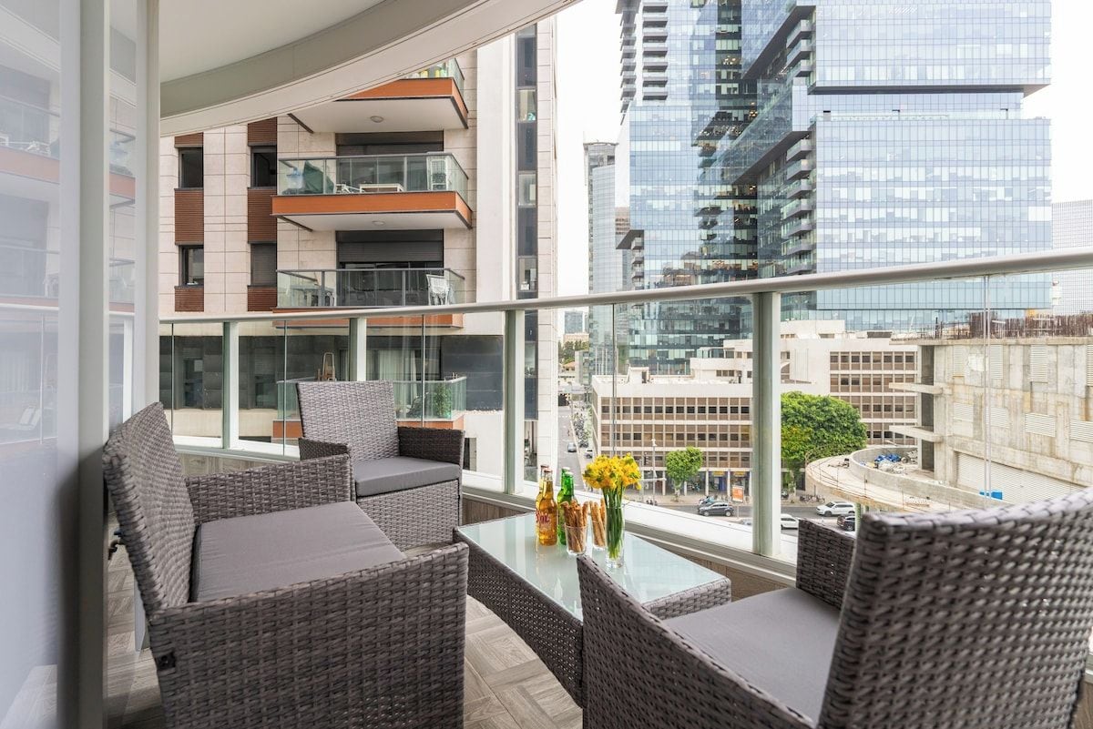 A balcony with wicker furniture, a glass table, and a view of the cityscape.