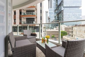 Un balcon agrémenté de meubles en osier, d’une table en verre et offrant une vue sur le paysage urbain.