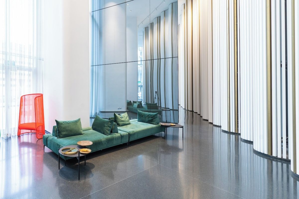 Ein modernes Interieur mit einem grünen Sofa, einem roten Sessel und einer spiegelnden Wand.